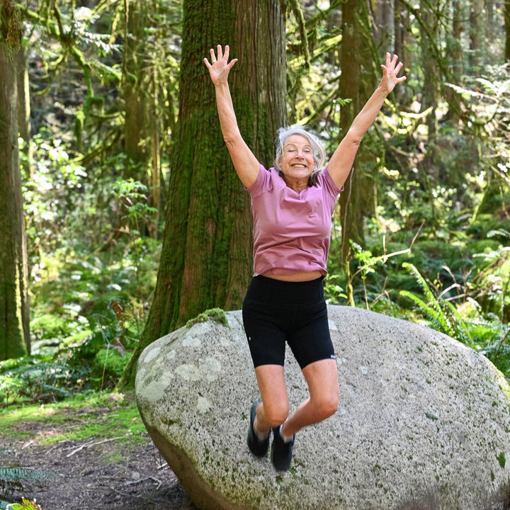 Person jumping off a large rock in a forest