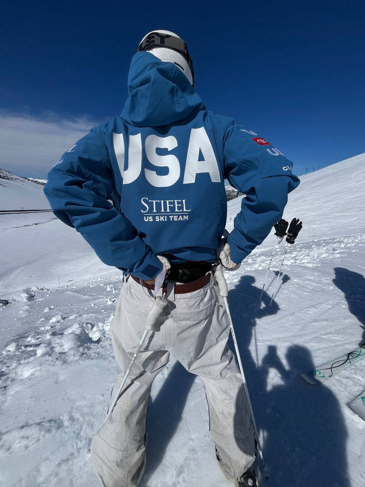 Person in a blue jacket with 'USA' and 'Stifel' branding on a snowy mountain