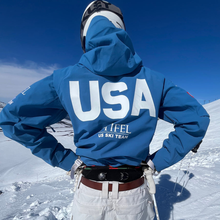 Person in a blue jacket with 'USA' on it, standing on a snowy landscape.